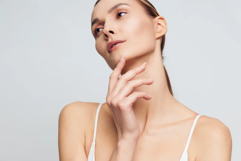 Portrait of a young woman with clear skin looking away thoughtfully, soft lighting, minimal makeup, natural expression, neutral background, close-up beauty shot