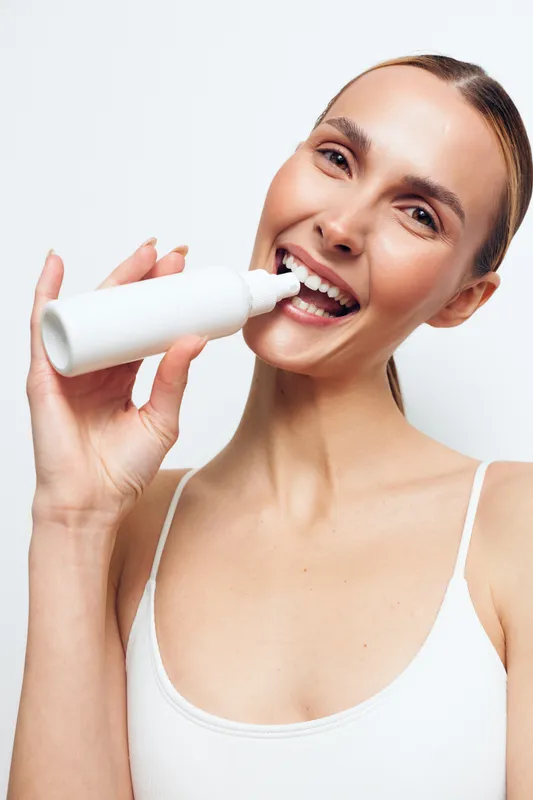 Smiling woman applying skincare cream to face, close up portrait on isolated white background, moisturizing treatment for beauty and wellness, minimal soft light