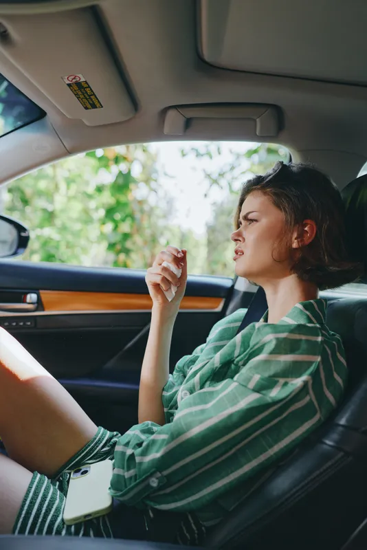 A woman sits in a car seat with a green striped shirt, natural light, relaxed posture, and a focused, contemplative expression in the cabin.