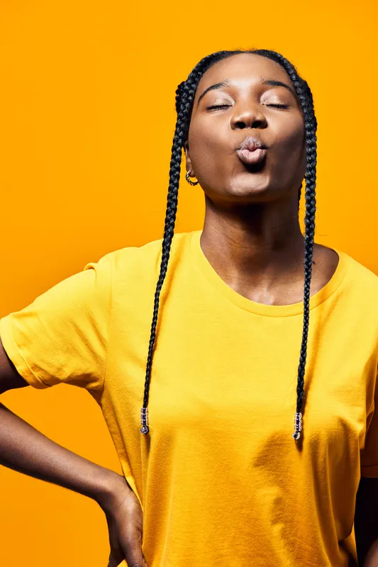Joyful African woman in yellow t shirt with playful expression against bright orange background, showcasing happiness and confidence