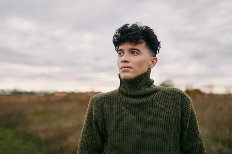 Close portrait of a young man in a turtleneck outdoors, natural lighting captures quiet confidence and subtle emotion, emphasizing authenticity and credibility in a relatable, honest scene.