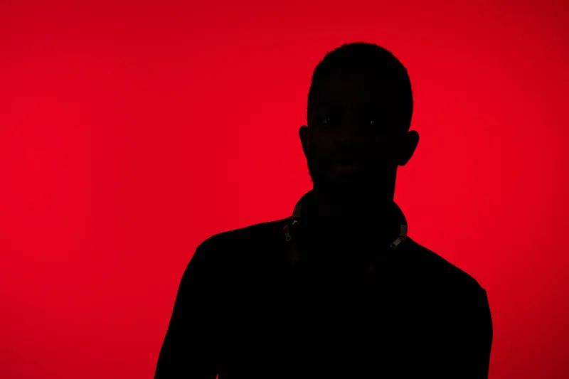 Silhouette of a young Black man with headphones against a vibrant red background, conveying a sense of mystery and creativity in urban music culture