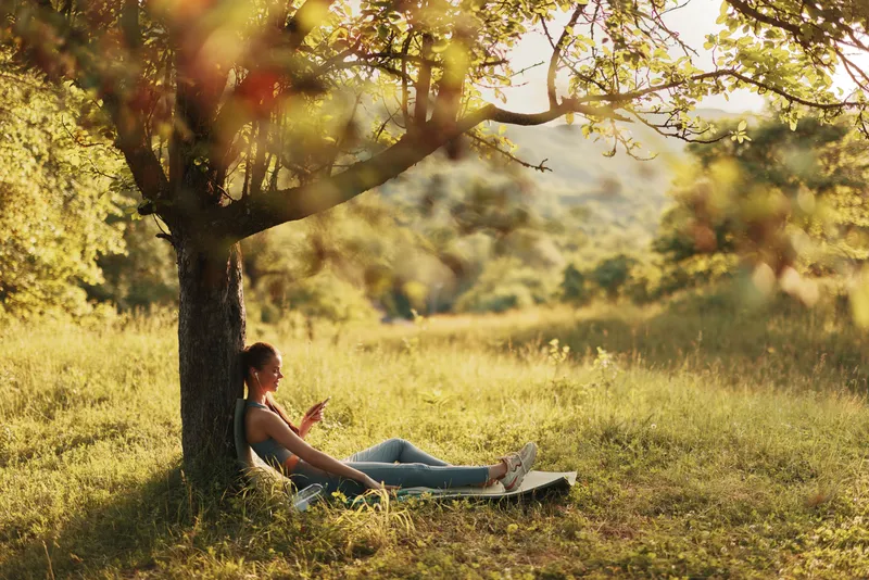 Young woman enjoying a peaceful moment under a tree in a lush green park, embracing nature, tranquility, and relaxation during a sunny day