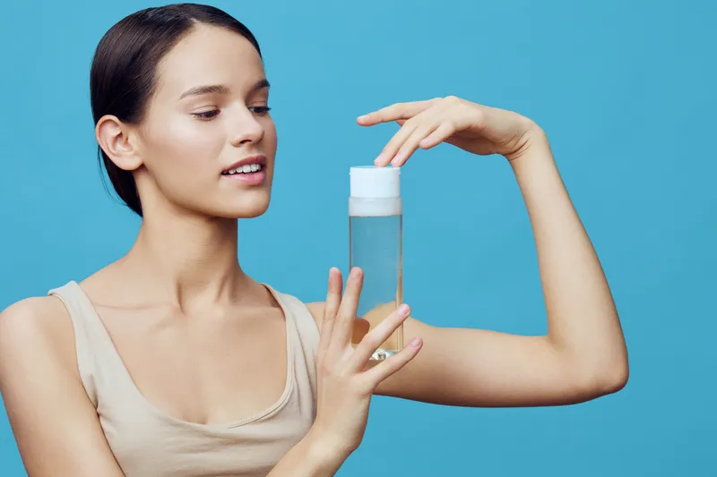 Young woman of mixed ethnicity showcasing a skincare product against a vibrant blue background, expressing joy and confidence in beauty care