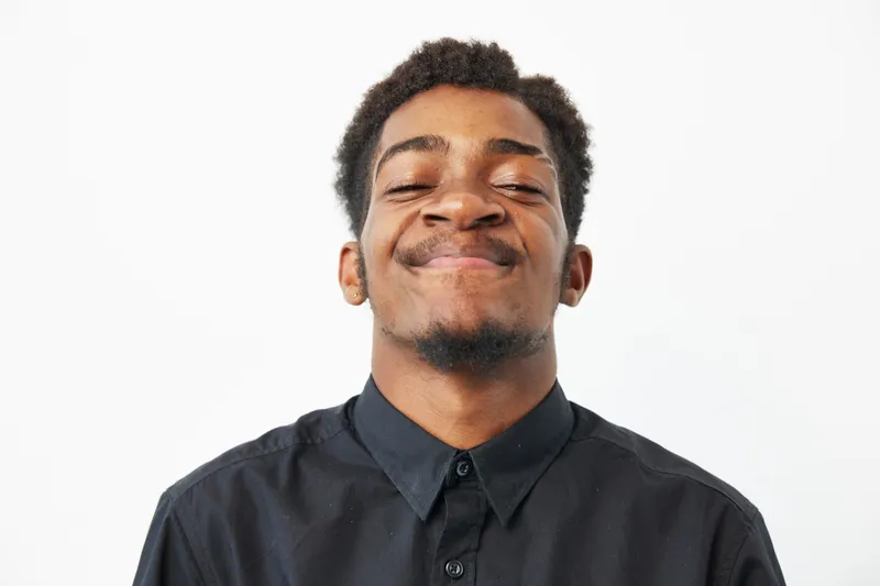 A joyful black man smiling brightly, showcasing happiness and confidence. His casual attire complements the bright background, perfect for lifestyle visuals.