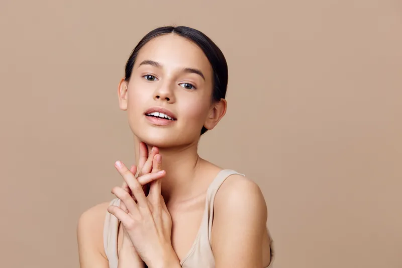 Young woman with natural makeup, smiling gently against a beige background, embodying beauty, confidence, and wellness in a minimalistic style