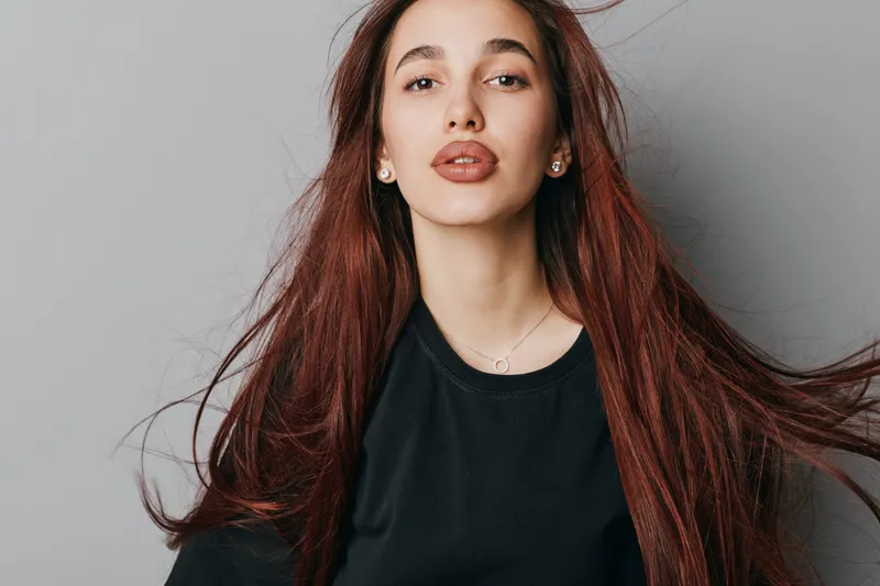 Young woman with long red hair and natural makeup posing in black shirt on neutral background for beauty, fashion and portrait photography concept.