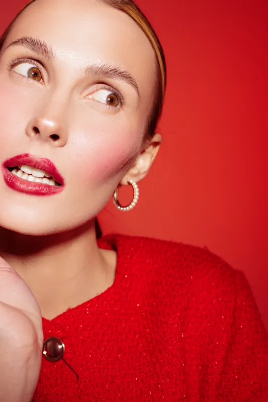 Close-up of a young woman with red lipstick and hoop earrings wearing a red sweater against a red background. Concept of fashion, beauty, and vibrant style.