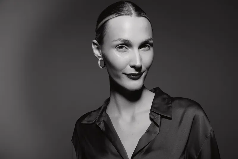 Portrait of a slender white woman with pale skin and slicked back hair wearing a dark blouse in black and white lighting.