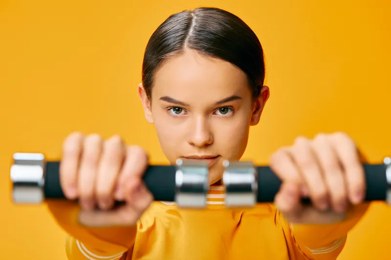 Fitness, woman and sport scene featuring a focused athlete gripping dumbbells against a bright orange background, highlighting workout intensity and strength training.