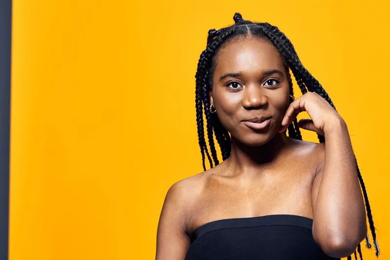 Confident young woman with braided hair in a black strapless top against a vibrant yellow background, showcasing self assurance and style