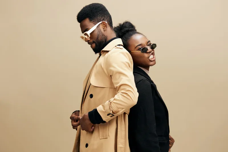 Stylish black couple in trendy outfits showcasing urban fashion, posing back to back with confidence and flair against a neutral backdrop