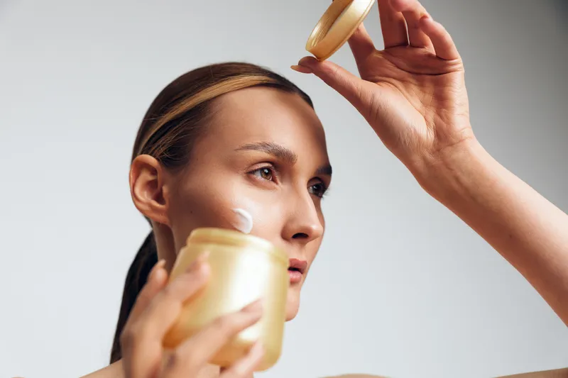 Woman skincare applying face cream with hand, using serum in a spa beauty routine indoors, closeup view, soft daylight, calm expression, smooth texture golden