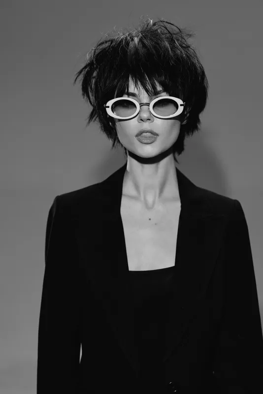 Black and white portrait of stylish woman with short hair wearing sunglasses and blazer in studio