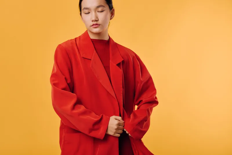 Young woman in red oversized jacket standing with closed eyes on yellow background fashion style casual expression calm and confident beauty portrait studio.