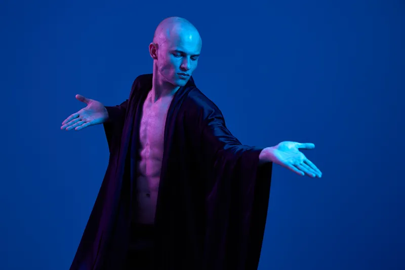 Dynamic man in flowing robes showcasing a captivating pose, accentuated by vivid blue lighting that creates an electrifying atmosphere.