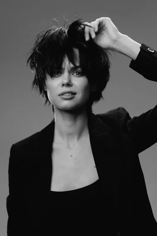 Black and white portrait of a woman with short messy hair wearing a black blazer expressing confidence and style.