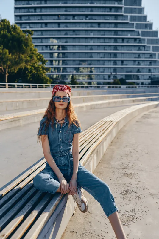lifestyle woman in modern boho-western denim street style sitting outdoors with sunglasses and bandana in warm natural light film color tone