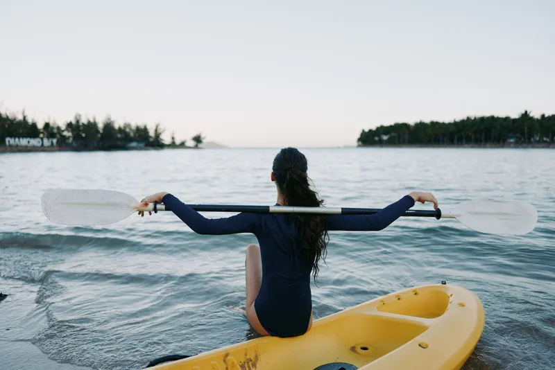 Woman holding paddle on yellow kayak in calm water at lake, relaxing during outdoor adventure with natural scenery and peaceful mood.
