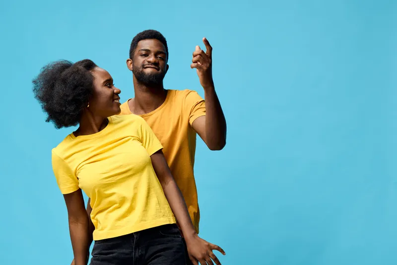 Happy young Black couple enjoying a fun moment together, wearing bright yellow shirts, against a vibrant blue background