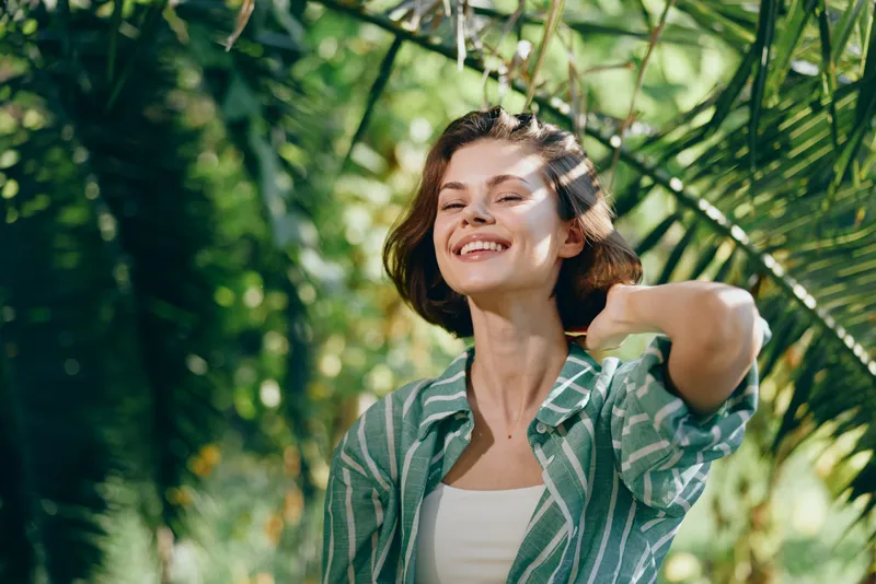 woman, smile, cheerful portrait of a woman outdoors among lush greenery, casual striped shirt, relaxed pose, warm sunlight, joyful mood, natural scene, confident vibe