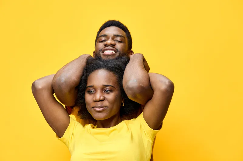 Happy African couple enjoying playful moments against a bright yellow background, showcasing vibrant emotions and casual summer style in matching yellow outfits