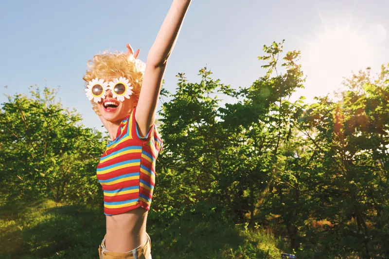 Joyful child outdoors, wearing a striped shirt and oversized sunglasses, arms raised in a sunlit moment, capturing playful energy with retro film color