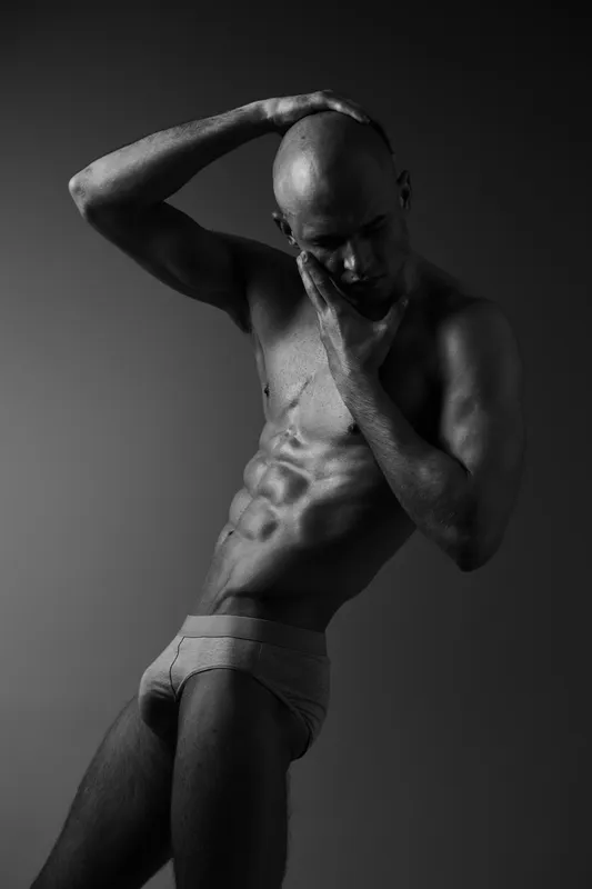 Sculpted man in striking black and white, showcasing athletic physique and emotional expression against a minimalistic background, embodying strength and vulnerability.