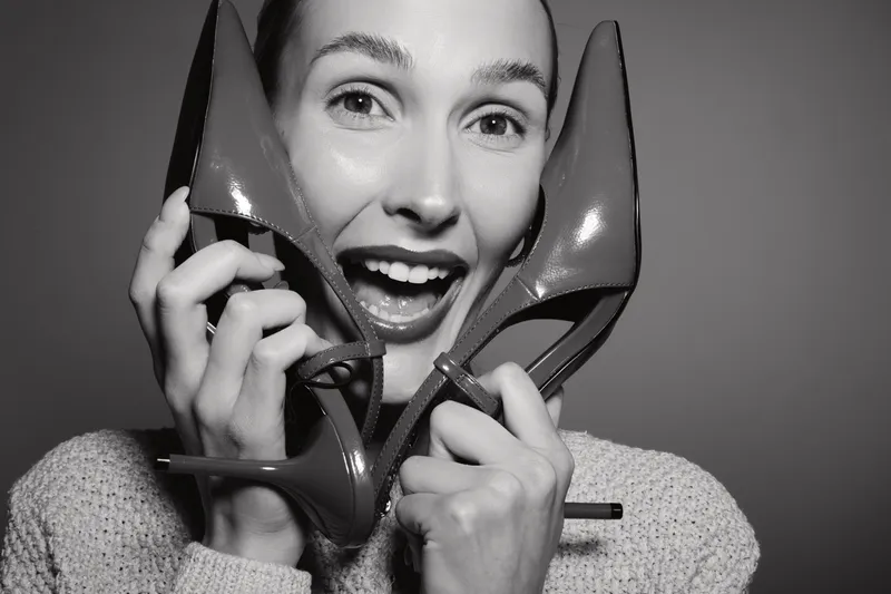 Happy Caucasian woman with light skin holds red high heel shoes near face smiling. Concept for fashion, style, beauty, and footwear accessory in studio.