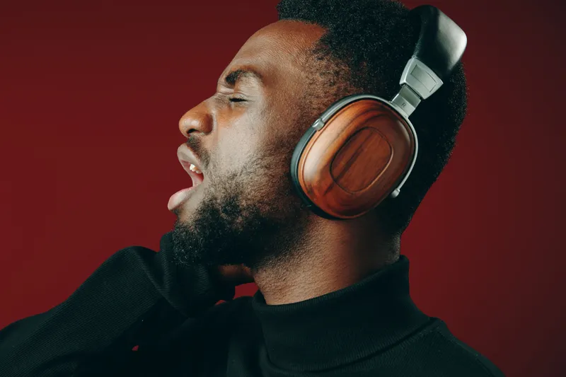 Portrait of a Black man wearing wooden headphones, passionately singing against a vibrant red background, showcasing emotions of joy and creativity