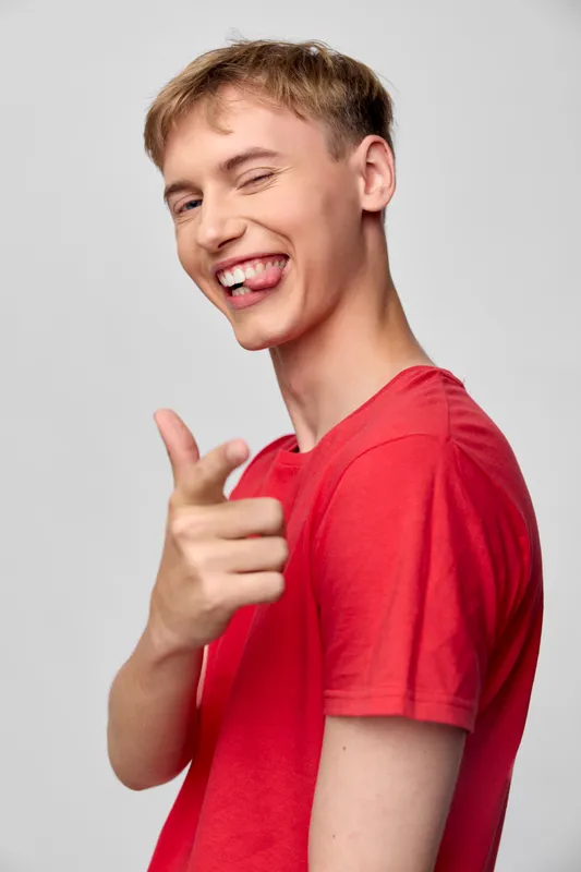 Smiling young man in a red shirt points playfully at the camera, conveying confidence, energy, and fun. A casual, friendly pose suitable for lifestyle, youth branding, and social media campaigns.