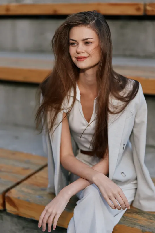 Confident businesswoman in casual chic attire, showcasing professionalism and elegance while sitting outdoors on wooden steps with natural background.