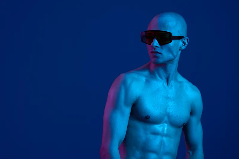 Abstract portrait of a man wearing futuristic sunglasses against a blue background, showcasing a blend of artistic lighting and colors that evoke a modern vibe.