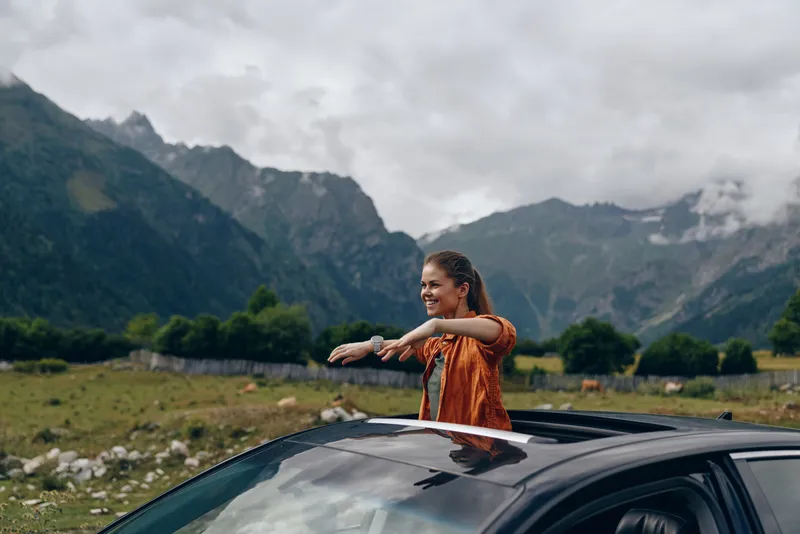 Woman car sunroof happy in mountains travel nature scene authenticity inclusivity