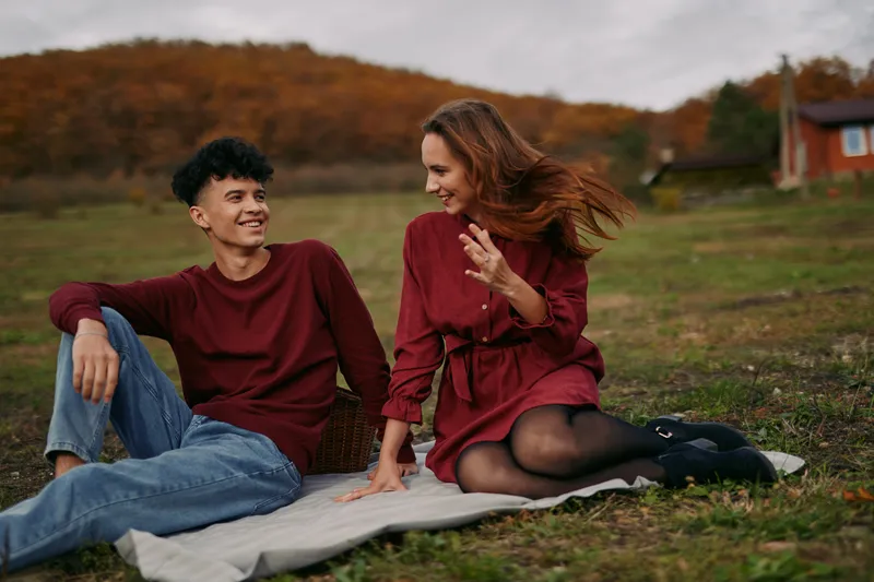 [Candid outdoor portrait of a young couple on a blanket in an autumn field, sharing a warm, genuine moment that emphasizes authenticity and emotional credibility.]