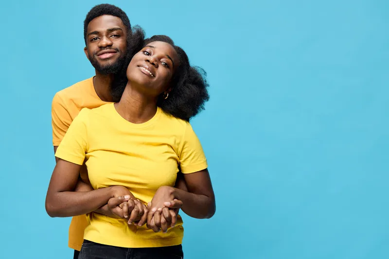 Happy young couple embracing with playful expressions against a bright blue background, showcasing love and joy in vibrant yellow shirts