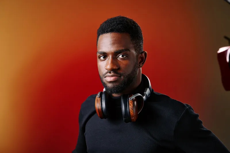 Confident young Black man wearing headphones against a vibrant gradient background, exuding focus and creativity in a modern lifestyle