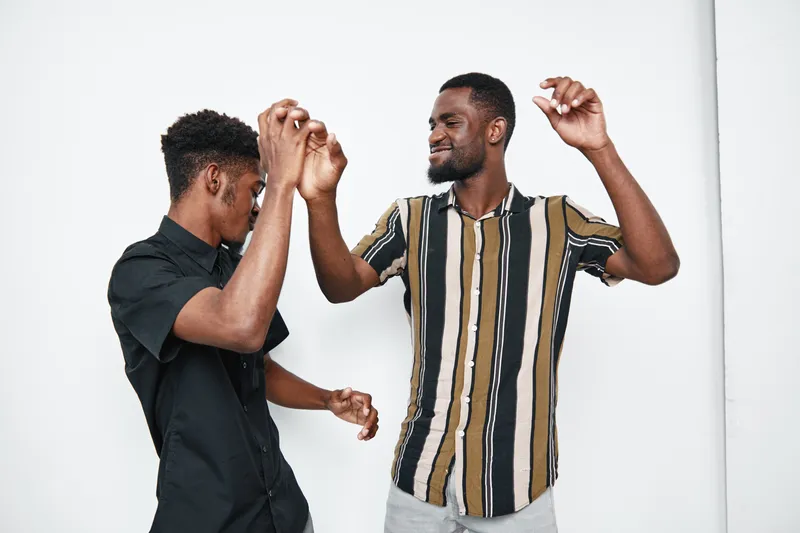 Two young black men dancing and having fun together in casual clothes with joyful expressions on white background. Friends enjoying music and movement indoors.