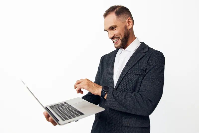 A confident business professional man operates a laptop, presenting a friendly smile and focus, against an isolated colored backdrop. He conveys motivation and readiness for strategy and