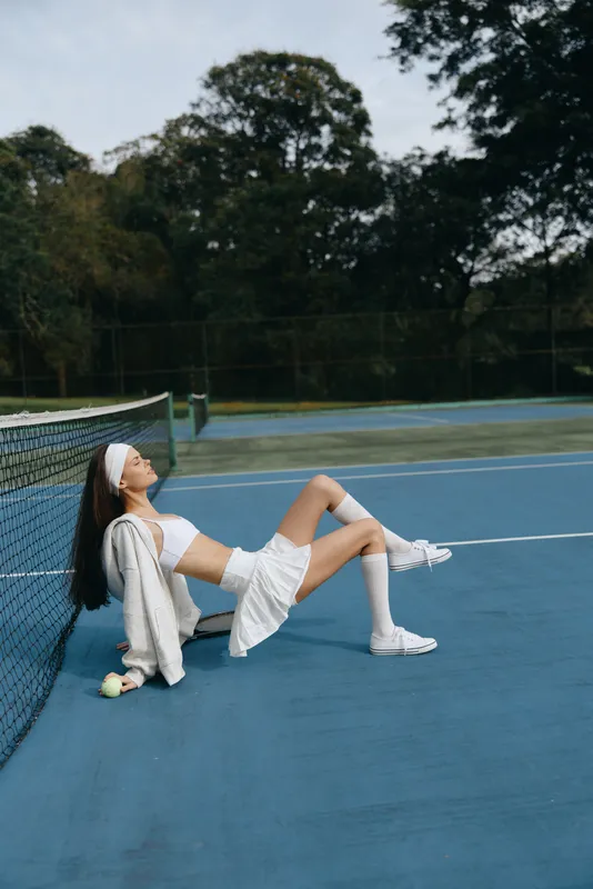 Athletic young woman relaxing on a tennis court, wearing sporty white apparel and expressing joy on a sunny day after a match, showcasing healthy lifestyle and sports enthusiasm