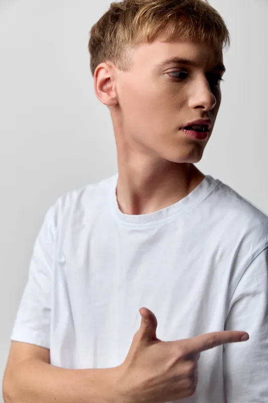 Man wearing a white shirt points to the side, showing a confident gesture and casual style for fashion, advertising, marketing, or presentation use in stock photography