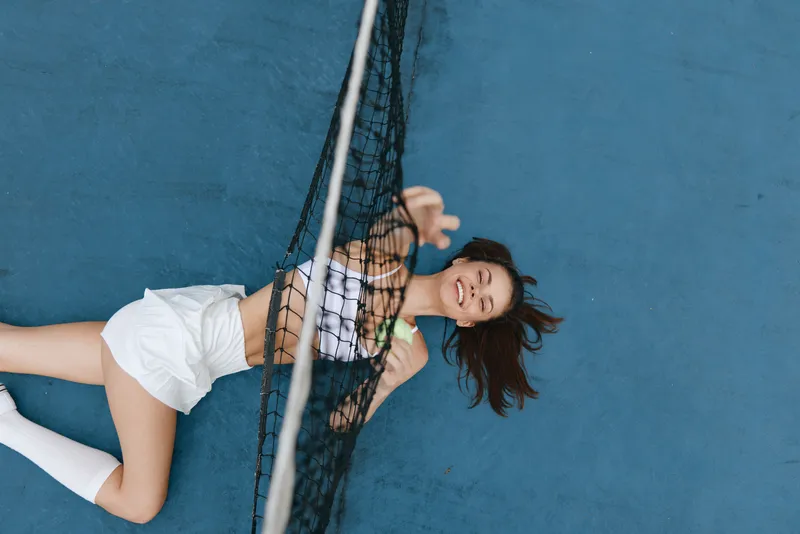 Young woman in sports attire joyfully stretching on a tennis court, showcasing athleticism and vibrant energy in a dynamic outdoor setting