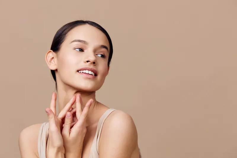 Young woman with smooth skin smiling gracefully on a beige background, showcasing natural beauty and elegance, ideal for wellness and beauty concepts