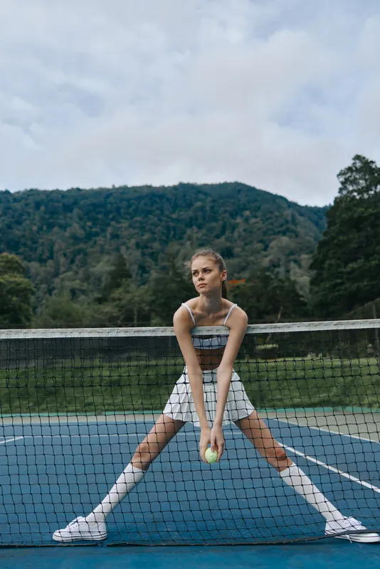Young female tennis player in athletic wear, exhibiting determination on a court with mountains in the background, perfect for sports and fitness promotion