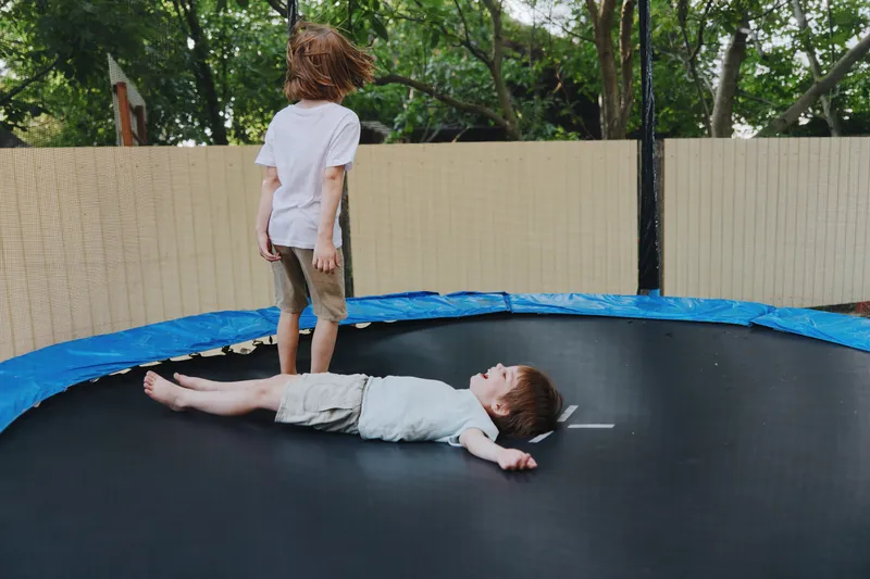 Two playful boys on a trampoline, one standing and the other lying down, capturing the fun spirit of childhood activities and outdoor playfulness.