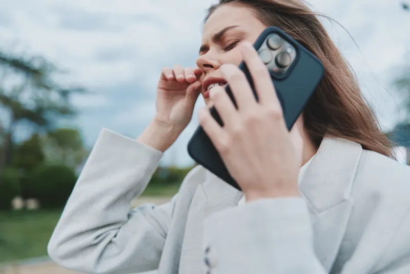 Confident businesswoman on the phone, expressing frustration while dressed in a stylish blazer against a dynamic outdoor background with a moody sky.