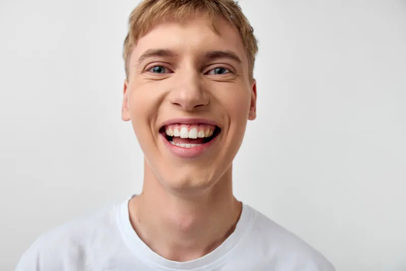 Bright close up of a smiling young man in a white shirt, radiating warmth and positivity for lifestyle, wellness and everyday joy in promotional visuals and advertising campaigns