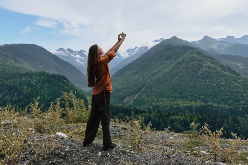 Outdoors mountains landscape photography nature traveler on a rocky overlook, capturing a panoramic view with a camera, conveying adventure and freedom