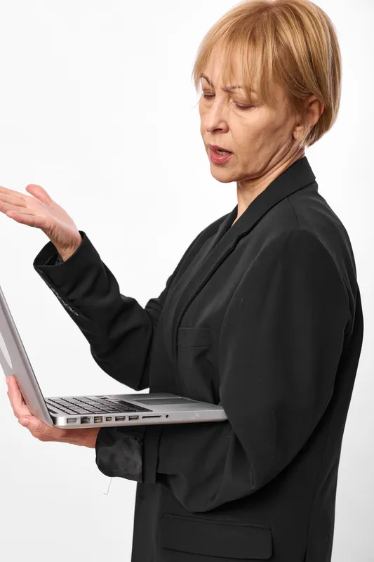 Older businesswoman, anger and frustration, holding laptop and making gesture, workplace stress in office, white studio background, concept of technical error, work