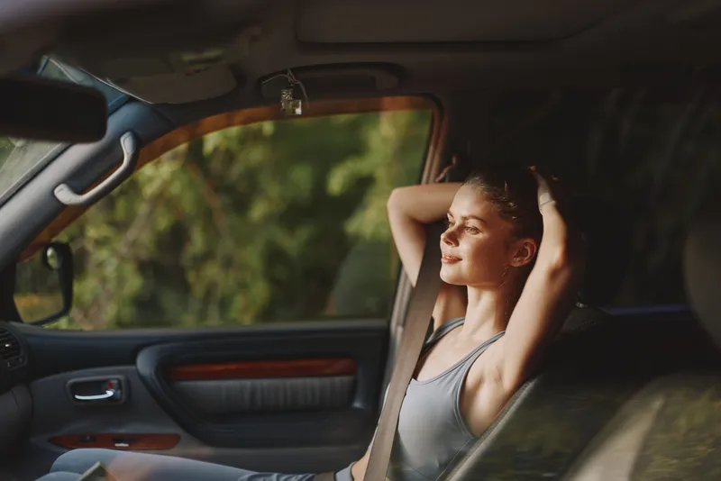 Young woman enjoying tranquility in a car, with a relaxed expression, wearing a casual outfit, surrounded by nature in a warm toned setting, ideal for concepts of relaxation and freedom